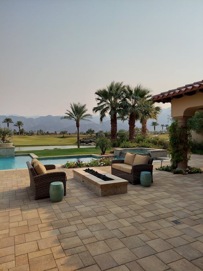 Serene outdoor patio with pool, wicker seating, and palm trees against mountain backdrop.